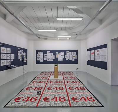 Blick in die Ausstellung im aut mit Geldteppich und Audiocollage "Wohnung? – Leider nein!" (Raum) und Hintergrundinformationen zur Ökonomie des Wohnens in Tirol