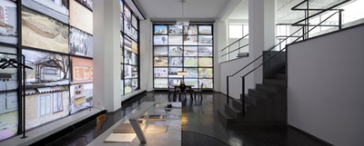 Blick in die Ausstellung "Amol eppas ondorsch", im Vordergrund Sparkassentisch mit Weinlicht (ANGO), im Hintergrund Stube Lanz (MAYMA)